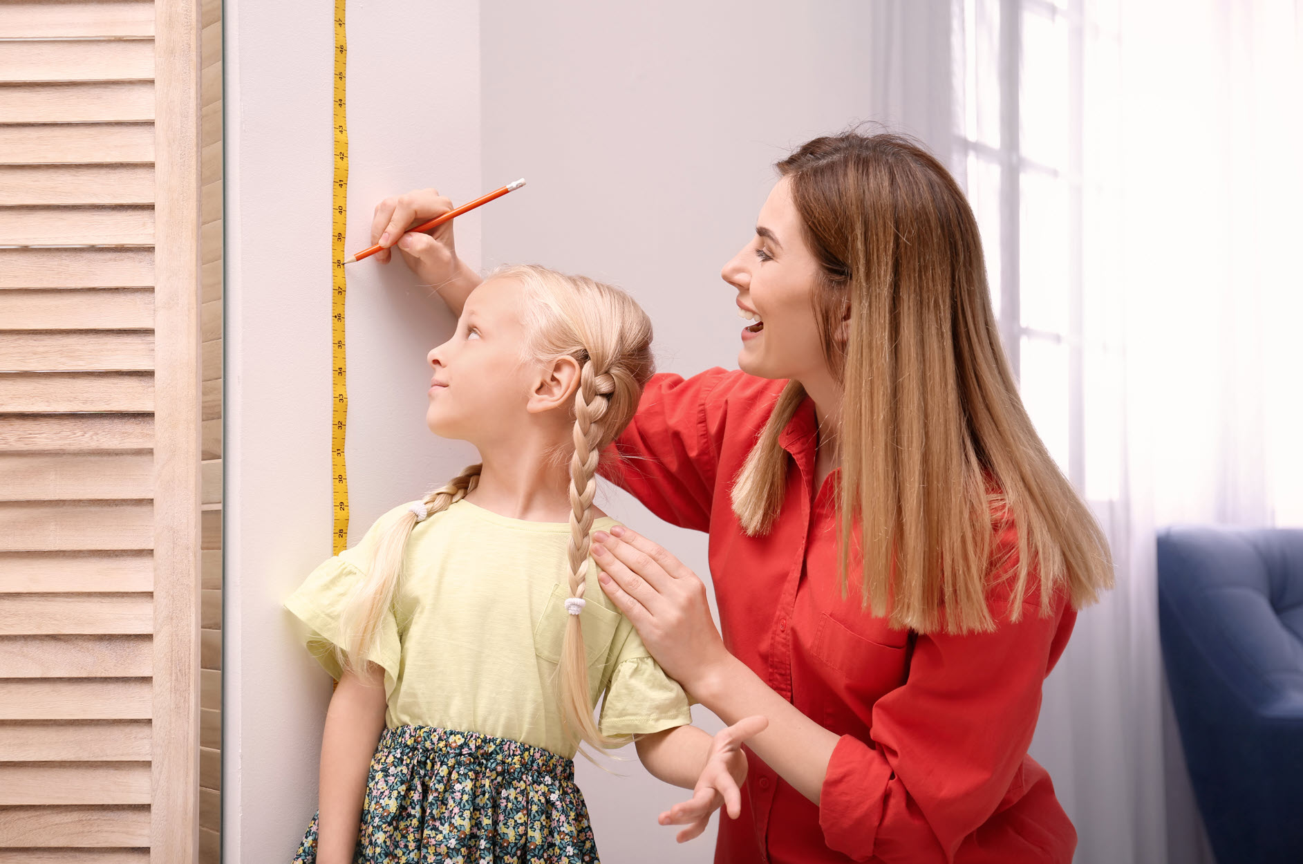 A mother measuring her daughter's growth against a wall