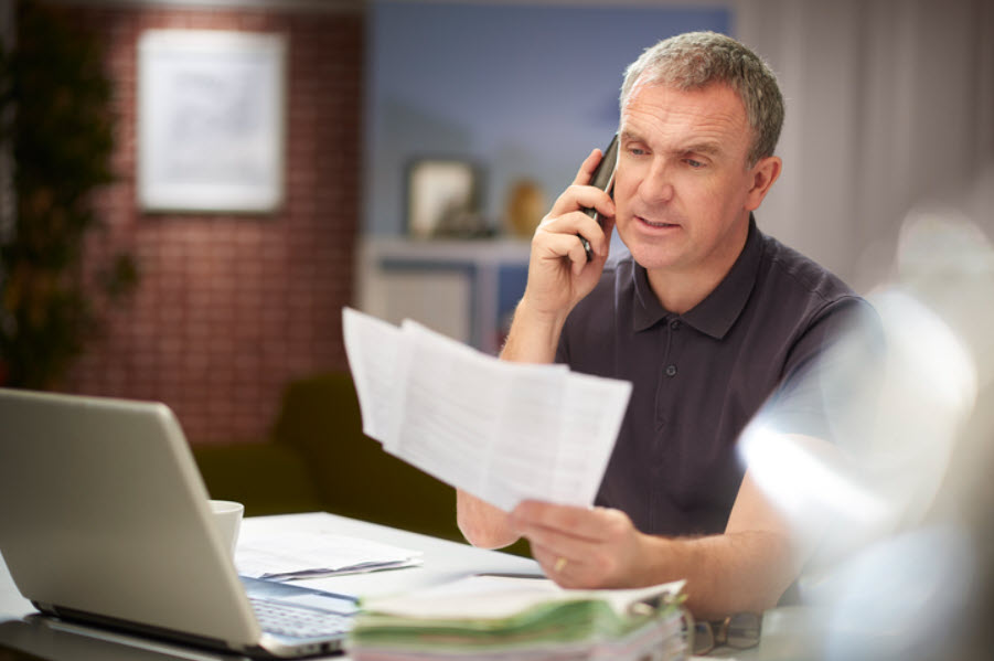 Man reviewing paperwork while speaking on the telephone